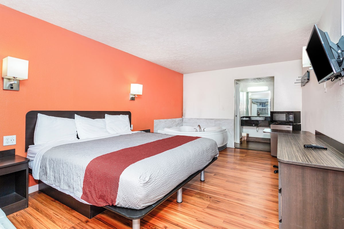 A hotel room with a bed, a desk, a TV, a bathroom, and a mirror.