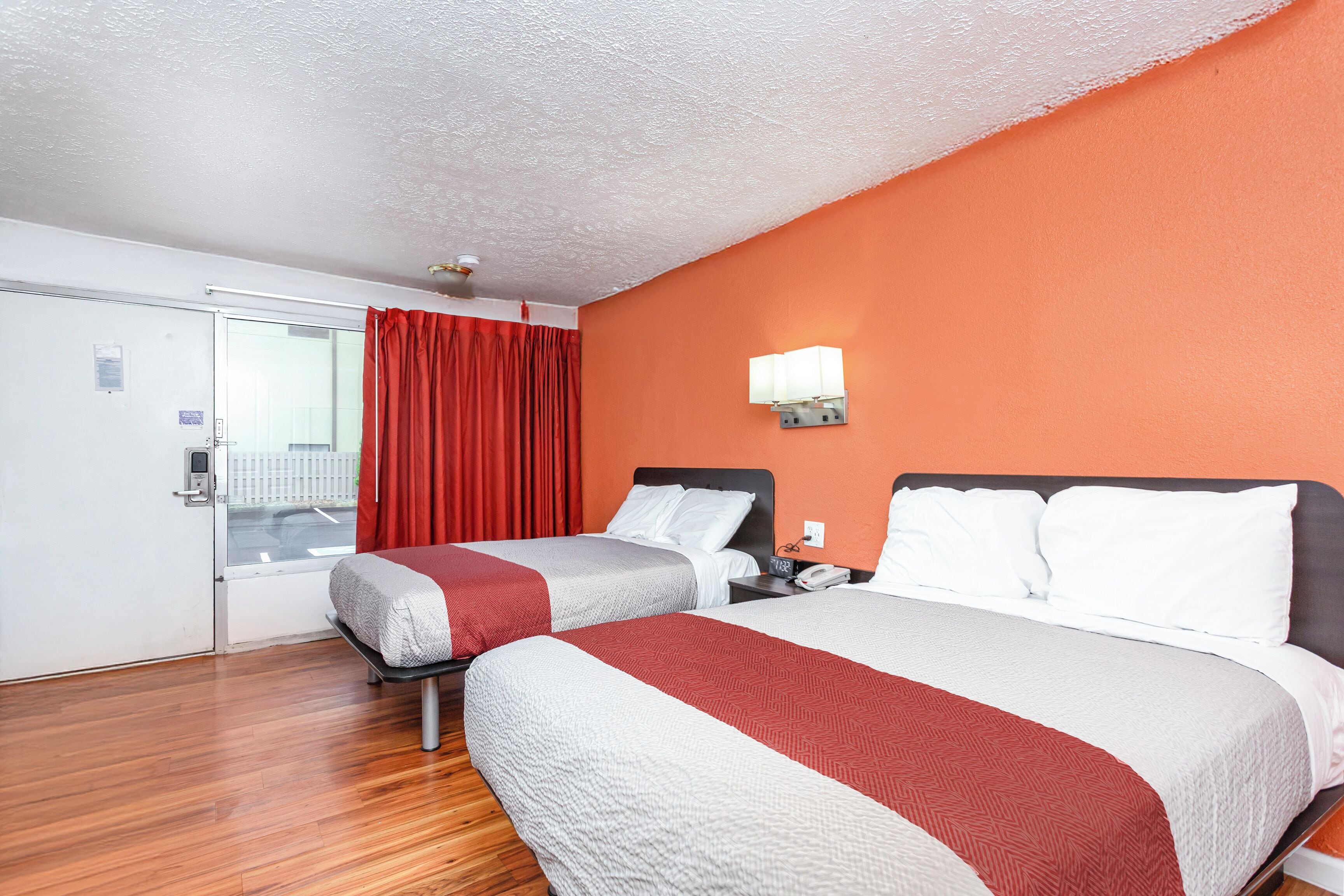 A hotel room with two beds, a red curtain, a white door, and an orange wall.