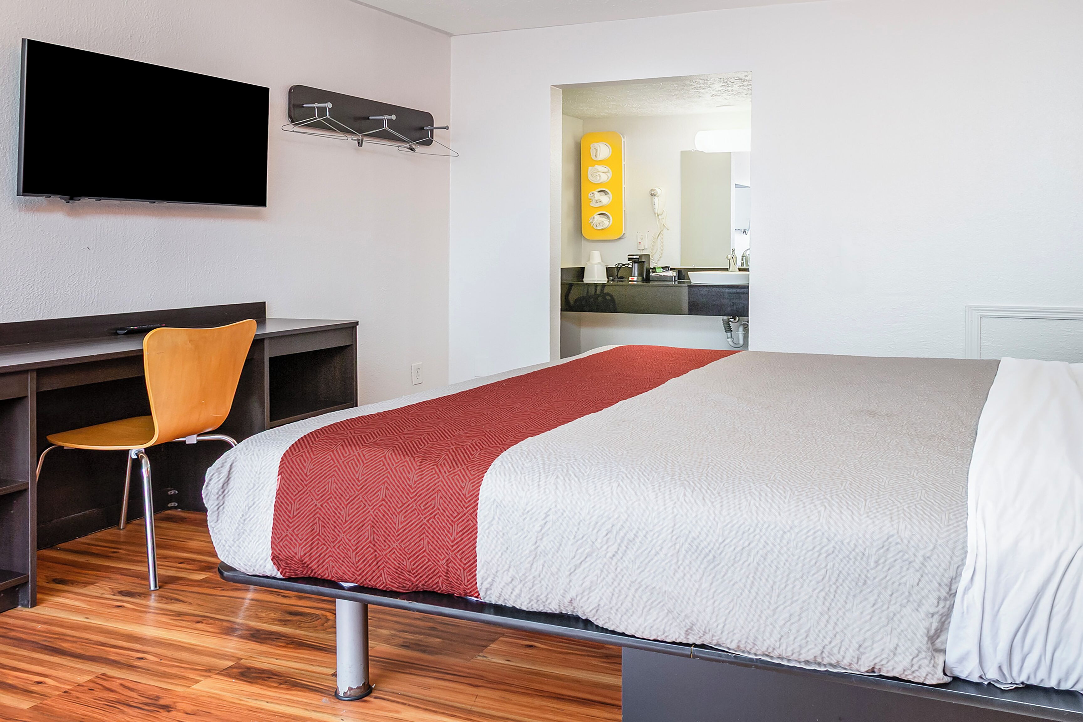 A hotel room with a bed, a desk, a chair, a TV, and a bathroom visible through an open door.