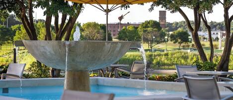 A pool area with a central water feature, lounge chairs, and an umbrella.