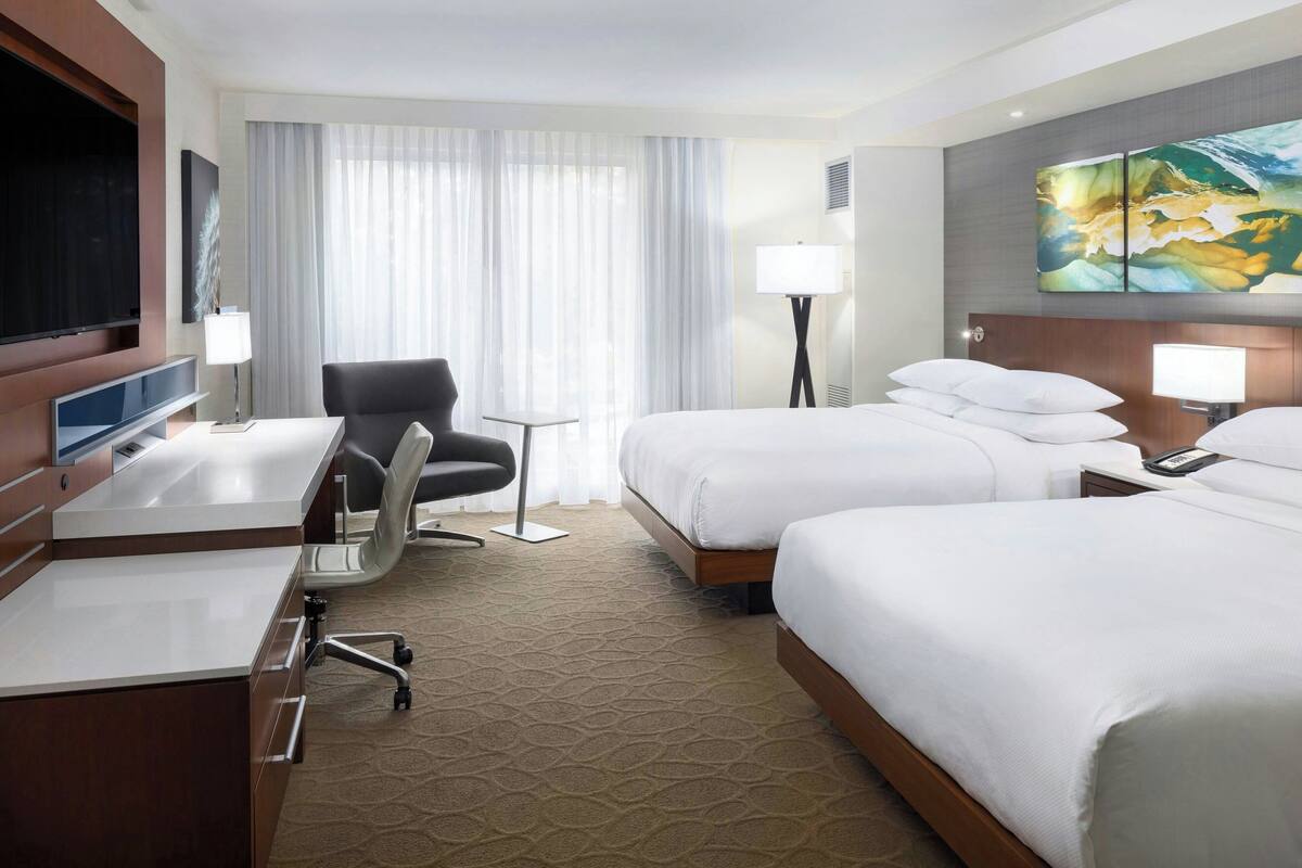 Ein Hotelzimmer mit einem großen Bett, einem Schreibtisch mit Stuhl, einem Fernseher und einem Bild an der Wand.