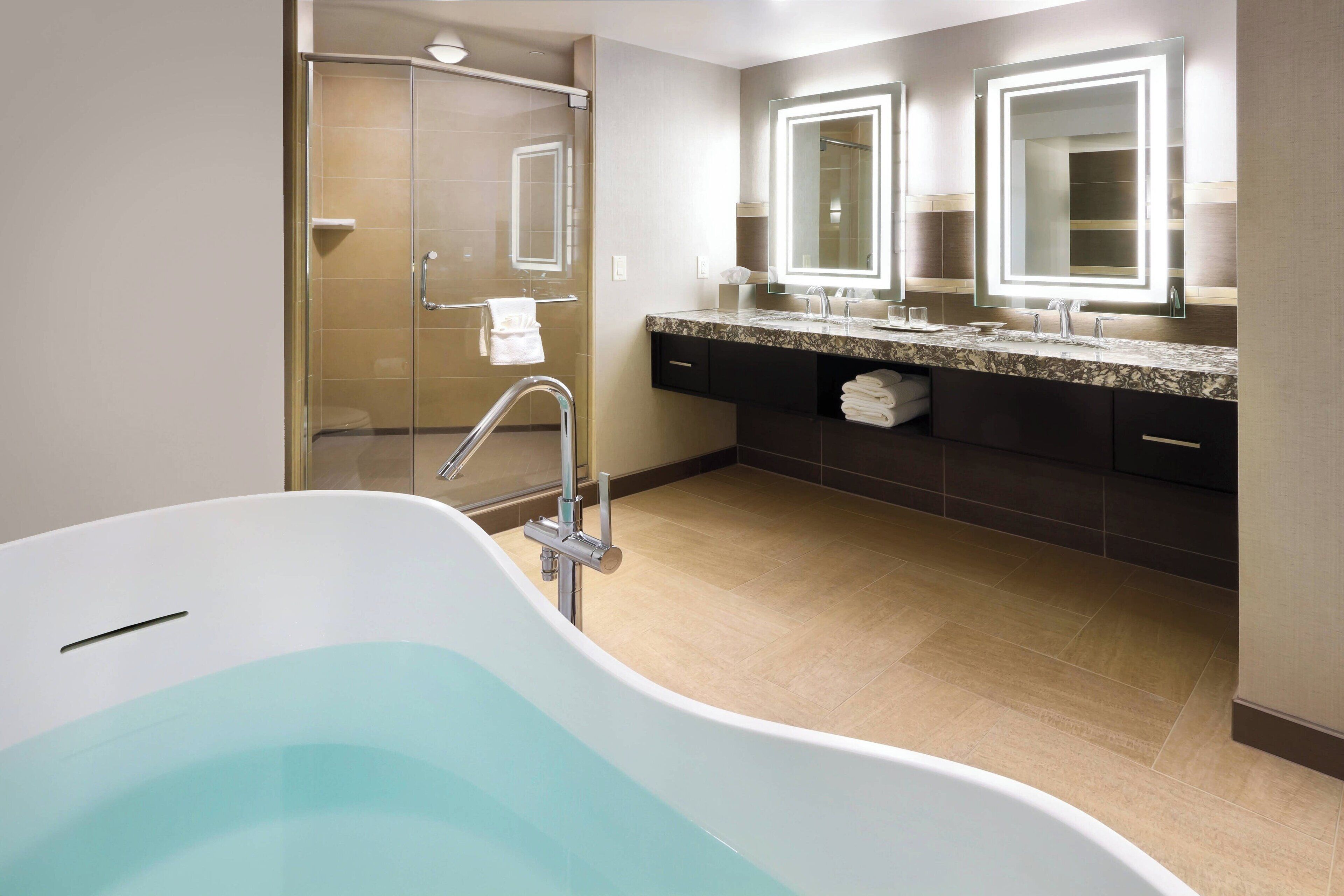 Un baño moderno con una bañera independiente, una ducha con mampara de vidrio y un lavamanos con dos espejos.