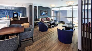 Un hall d’hôtel moderne doté d’un bar, d’un coin salon avec un téléviseur et de grandes fenêtres.