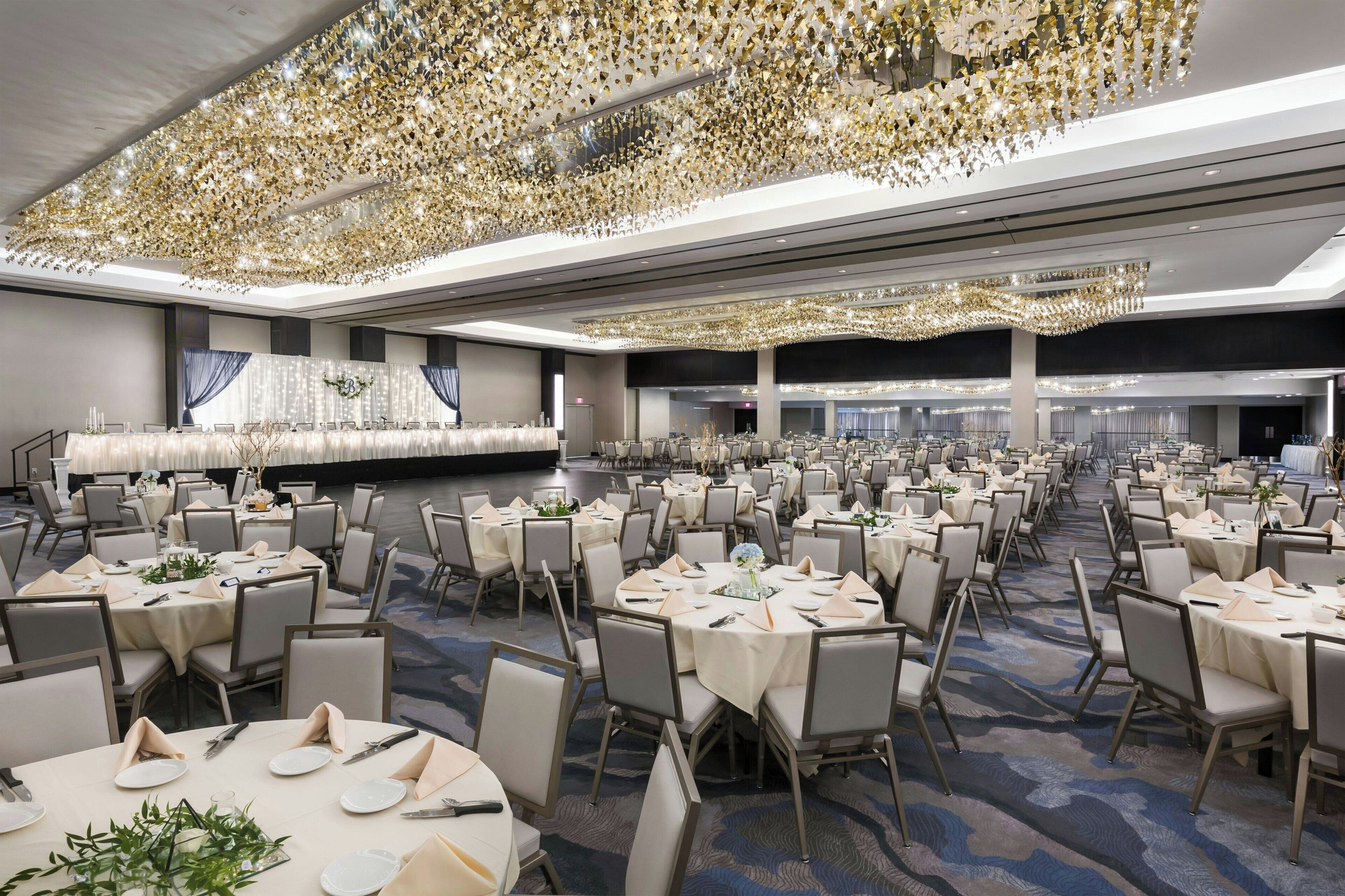 A spacious banquet hall with round tables set for dining, featuring a high ceiling with a decorative light fixture.