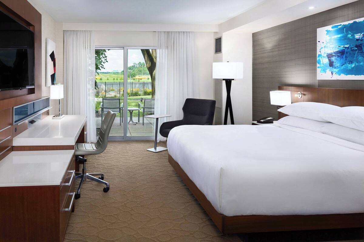 Ein Hotelzimmer mit Bett, Schreibtisch, Stuhl, Fernseher und Blick ins Freie.