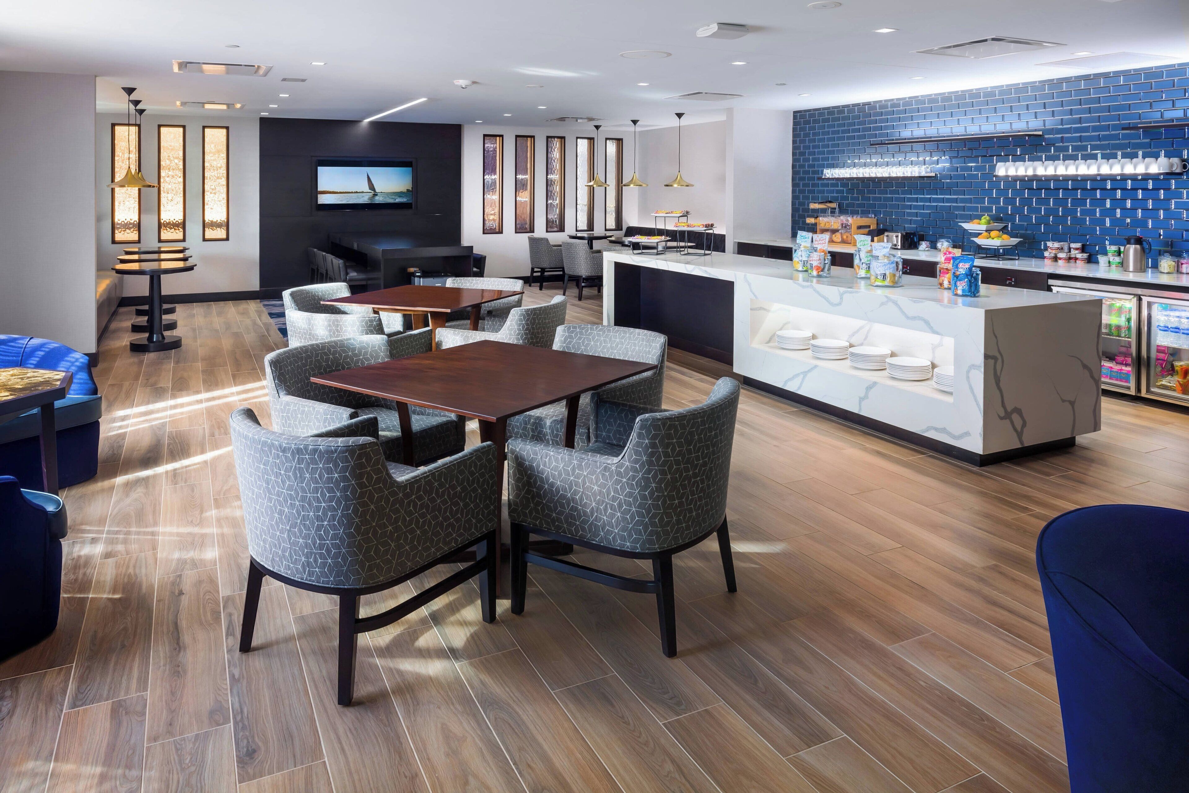 A modern hotel lobby with a bar area, seating arrangements, and a television screen.