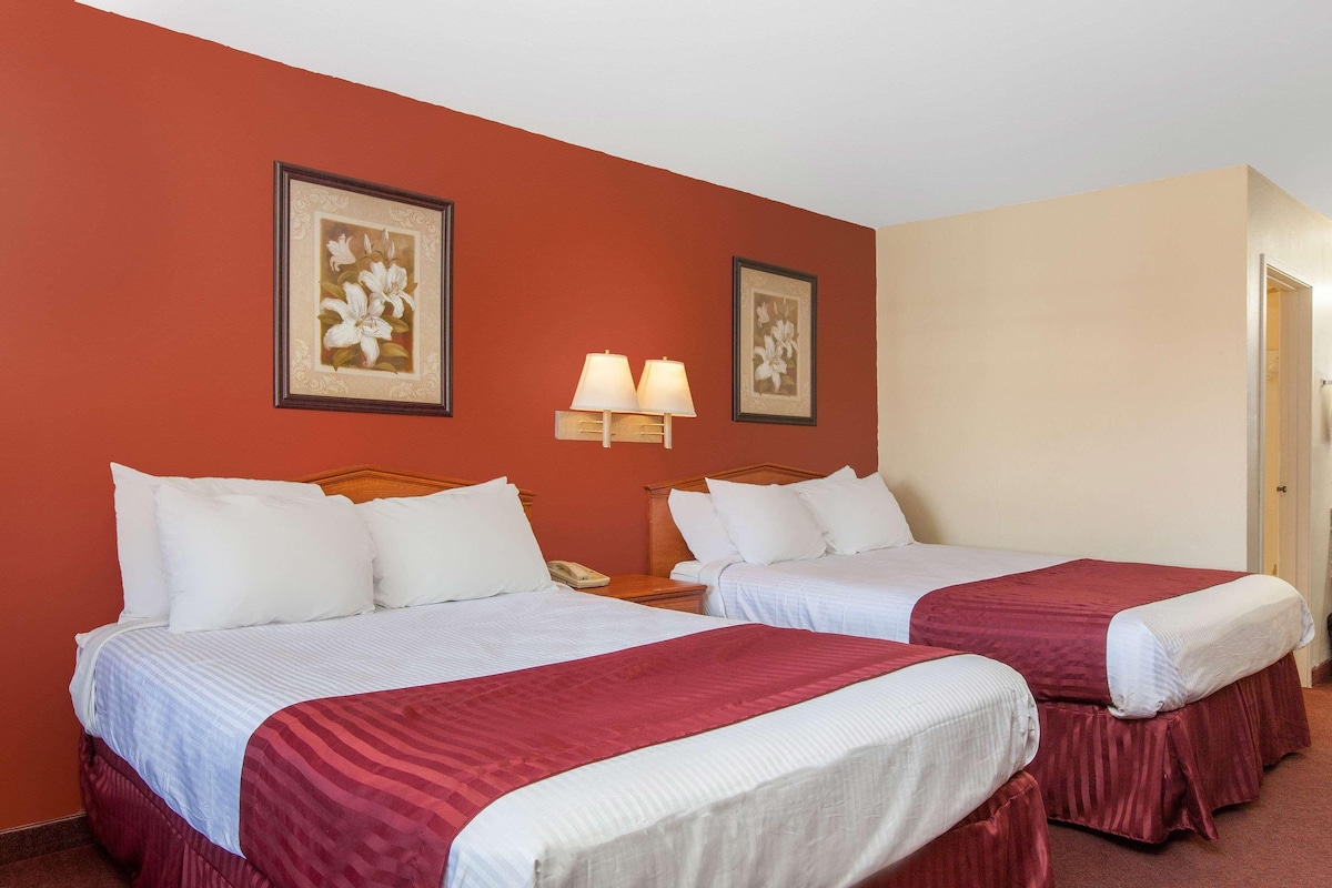 Habitación de hotel con dos camas, una mesita de noche con lámpara y dos cuadros con flores en la pared.
