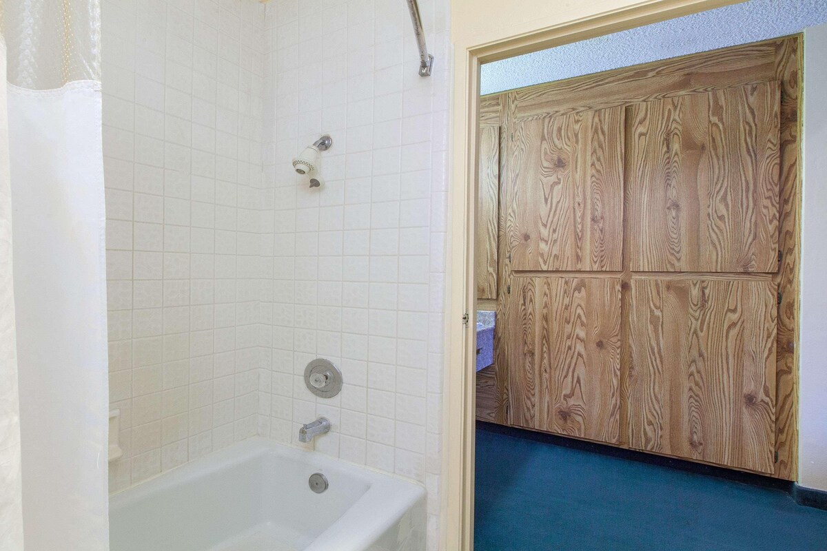 A bathroom with a bathtub, a showerhead, and a wooden door.