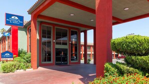 A hotel entrance with a red and green facade, large glass doors, and a covered outdoor area.