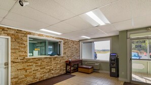 A reception area with a stone wall, a reception desk, an ATM, and a view of the outside. - Rodeway Inn Colonial Heights I-95 (Colonial Heights)