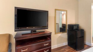 A living room with a flat-screen TV, a wooden entertainment unit, a black refrigerator, and a mirror on the wall. - Rodeway Inn Colonial Heights I-95 (Colonial Heights)