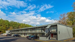 A motel with a two-story structure, a parking lot, and a forested hillside in the background. - Rodeway Inn Colonial Heights I-95 (Colonial Heights)