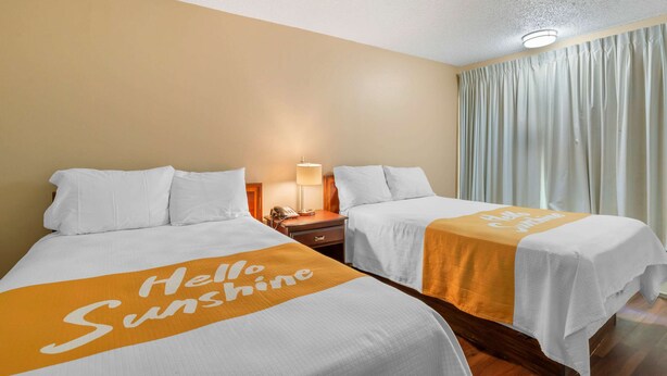 A hotel room with two beds, each with a 'Hello Sunshine' bedspread, a bedside table with a lamp, and a window with curtains. - Rodeway Inn Colonial Heights I-95 (Colonial Heights)