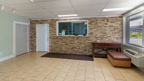 A reception area with a tiled floor, a reception desk, a bench, a window with a view, and a door. - Rodeway Inn Colonial Heights I-95 (Colonial Heights)