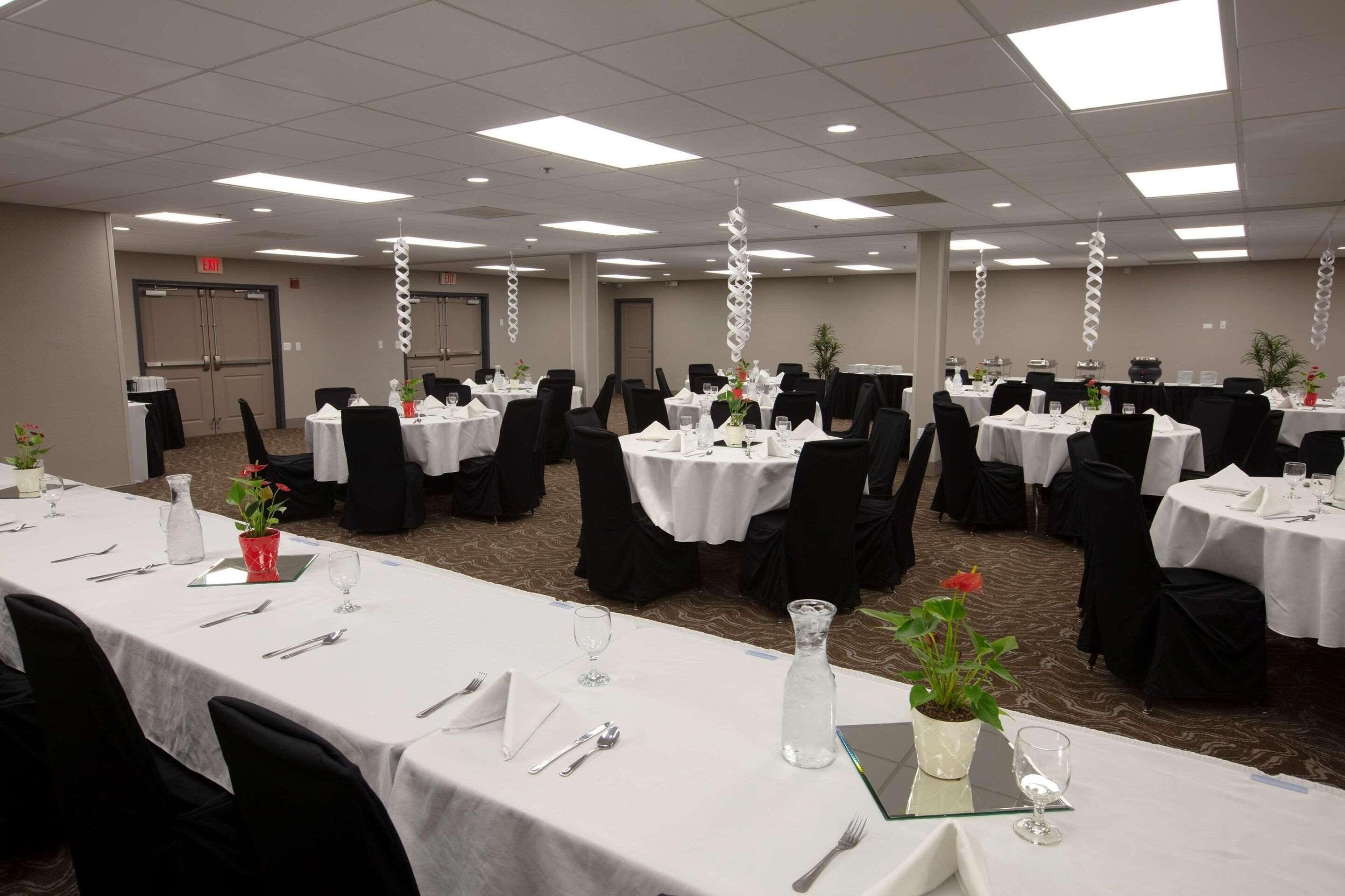 A banquet hall with multiple round tables set for dining, each with white tablecloths, black chairs, and centerpieces.