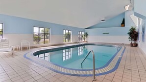An indoor swimming pool with clear blue water, surrounded by white chairs and potted plants. - Country Inn & Suites by Radisson, Fargo, ND (Fargo)