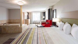 A hotel room with a large bed, a red armchair, a small table, a lamp, and a bathroom with a bathtub and sink. - Country Inn & Suites by Radisson, Fargo, ND (Fargo)