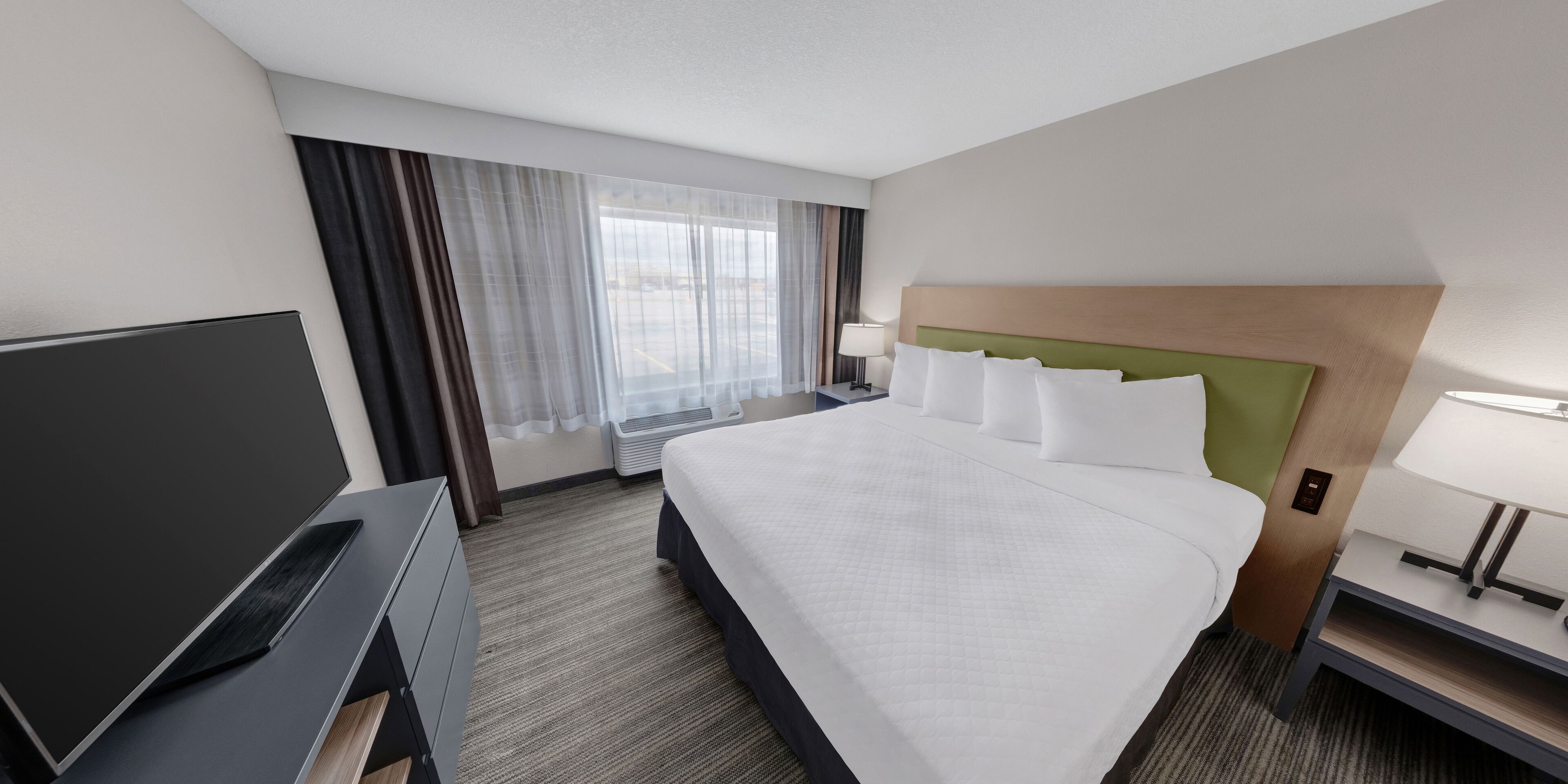 A hotel room with a large bed, a flat-screen TV, a desk, and a window with curtains.