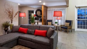 A living room with a grey sectional sofa, red and brown cushions, a wooden accent wall, a round clock, and two red lamps. - Country Inn & Suites by Radisson, Fargo, ND (Fargo)