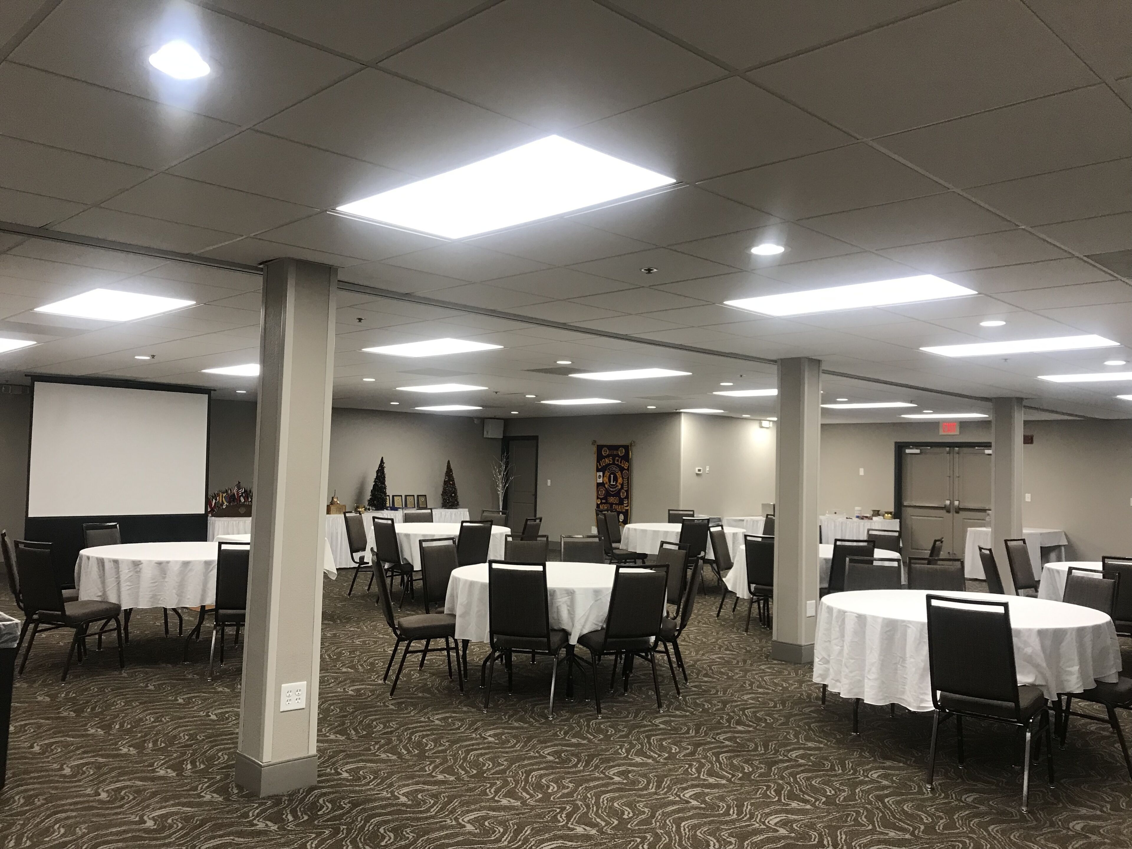 A conference room with multiple round tables, chairs, and a projector screen.