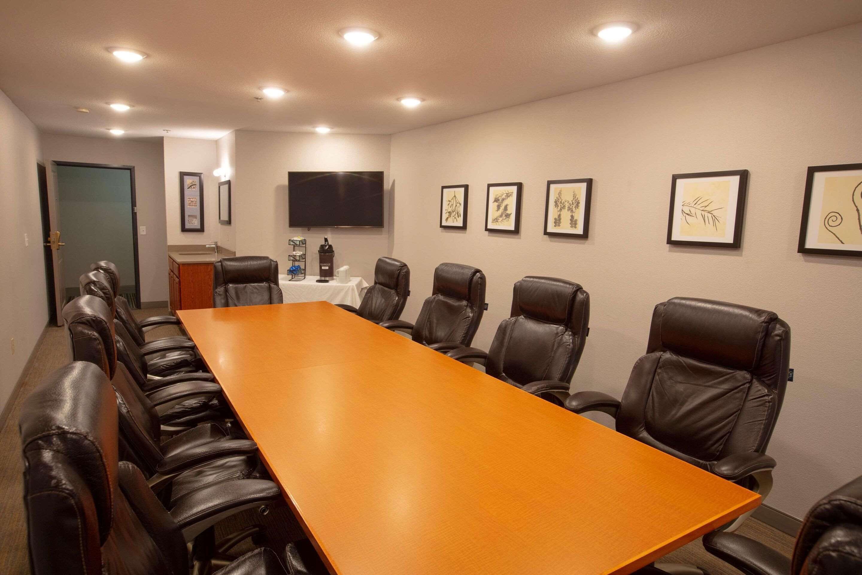 A conference room with a long wooden table and leather chairs, a flat-screen TV, and framed artwork on the walls.
