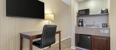 A hotel room with a flat-screen TV, a desk with a chair, a coffee maker, a microwave, and a mini-fridge.