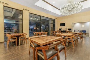 A spacious dining area with wooden tables and chairs, large windows, and a chandelier.