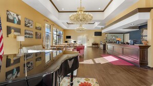 A spacious living area with a grand piano, a chandelier, and a large window offering a view of the outdoors. - Best Western Plus Big America (Santa Maria)