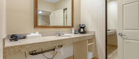 A bathroom with a granite countertop, a sink, a mirror, a hairdryer, a coffee maker, and a towel rack.