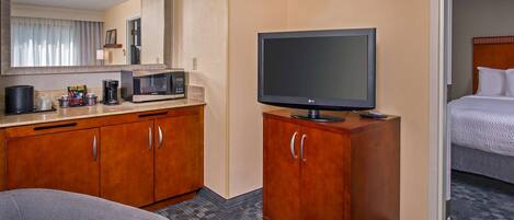 A hotel room with a bed, a TV on a wooden cabinet, a microwave, and a coffee maker on the counter.