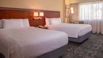 A hotel room with two beds, a nightstand with a phone, and a window with curtains.
