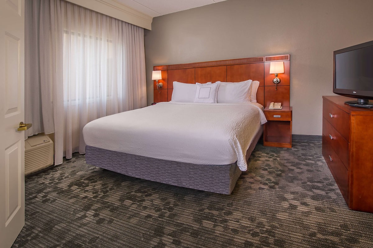 Ein Hotelzimmer mit einem großen Bett, zwei Nachttischlampen, einem Fernseher und einem Holznachttisch.