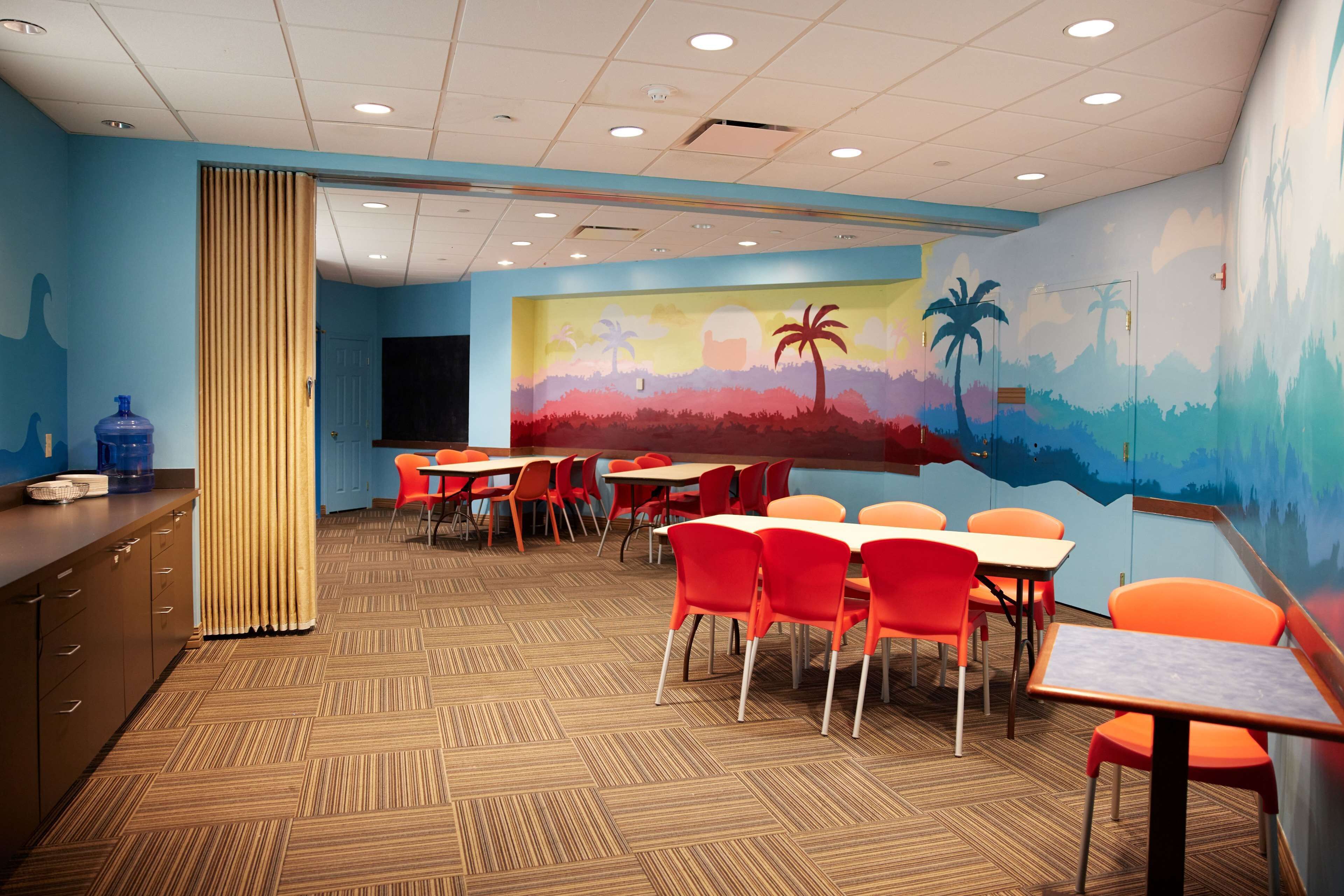 Un comedor con mesas y sillas, un dispensador de agua y un mural en la pared.