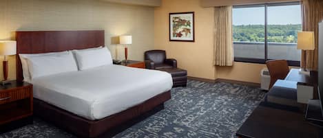 A hotel room with a large bed, a desk, a chair, and a view of the outdoors.