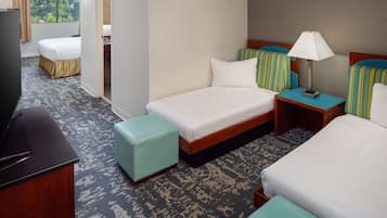 Habitación de hotel con dos camas, televisión, escritorio y ventana con vista a árboles.