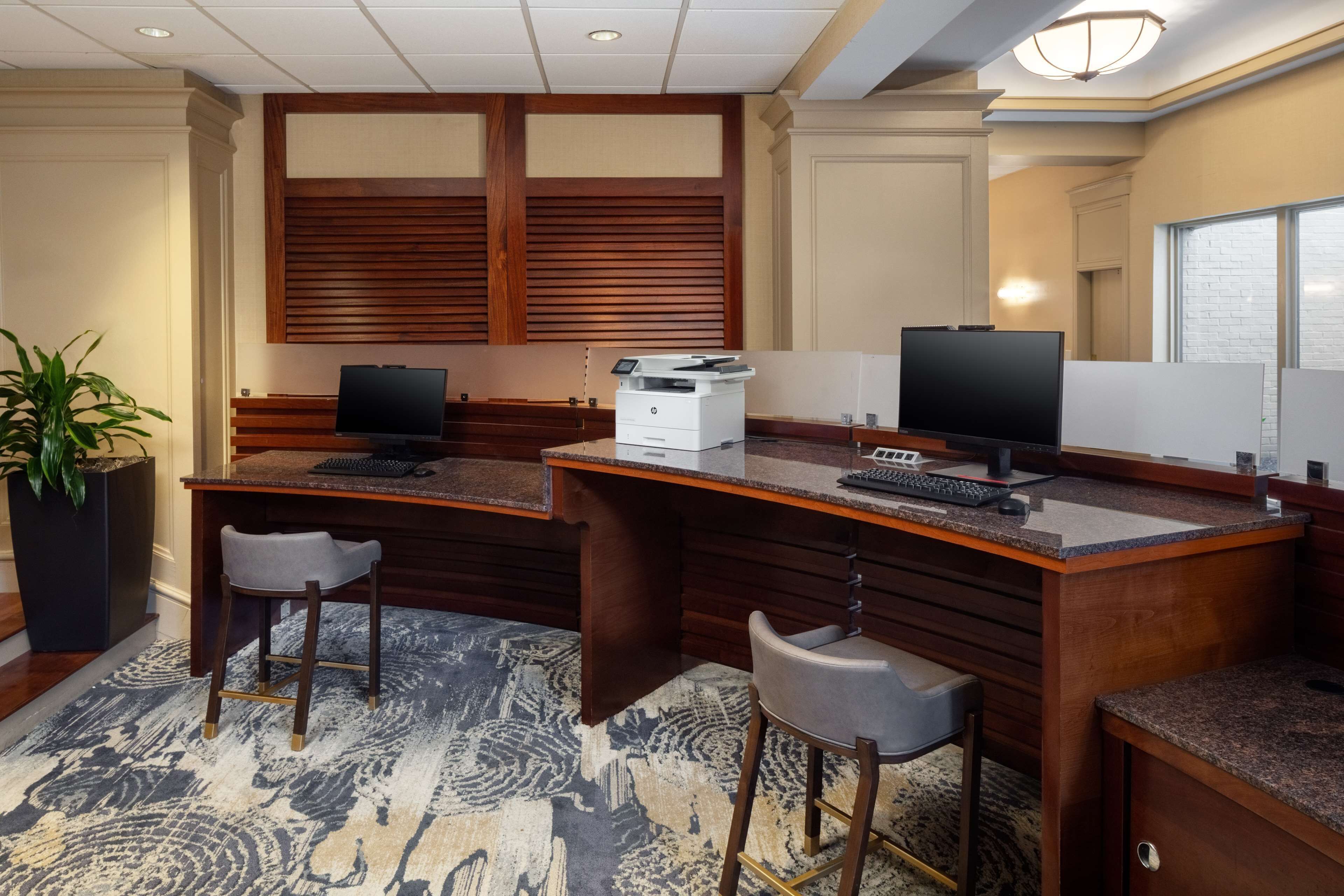 A hotel reception area with two desks, a large potted plant, and a patterned carpet.