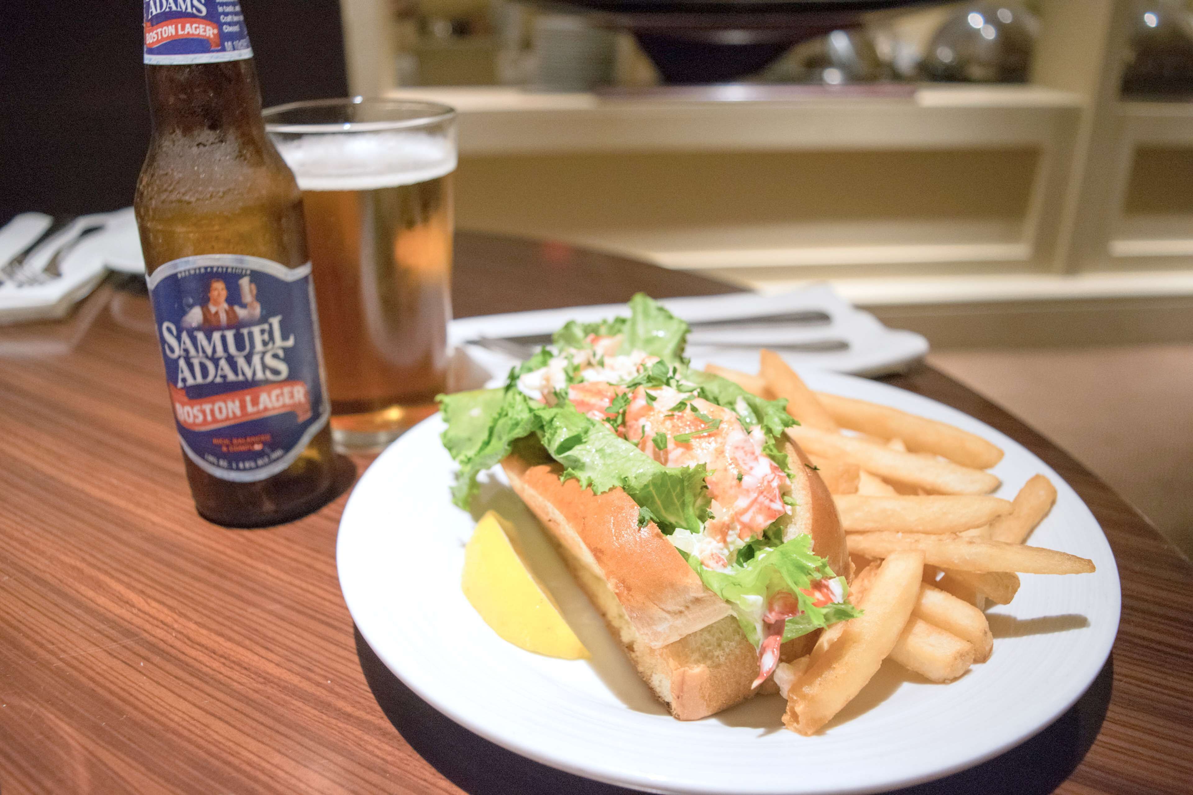 Een maaltijd bestaande uit een sandwich en friet, een glas bier en een fles bier op een tafel.