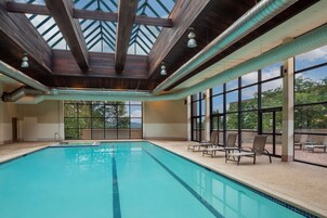 Una piscina interior con techo de tragaluces, ventanas amplias y sillones de descanso.