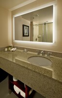 Un baño moderno con encimera de granito, un lavamanos y un espejo grande.
