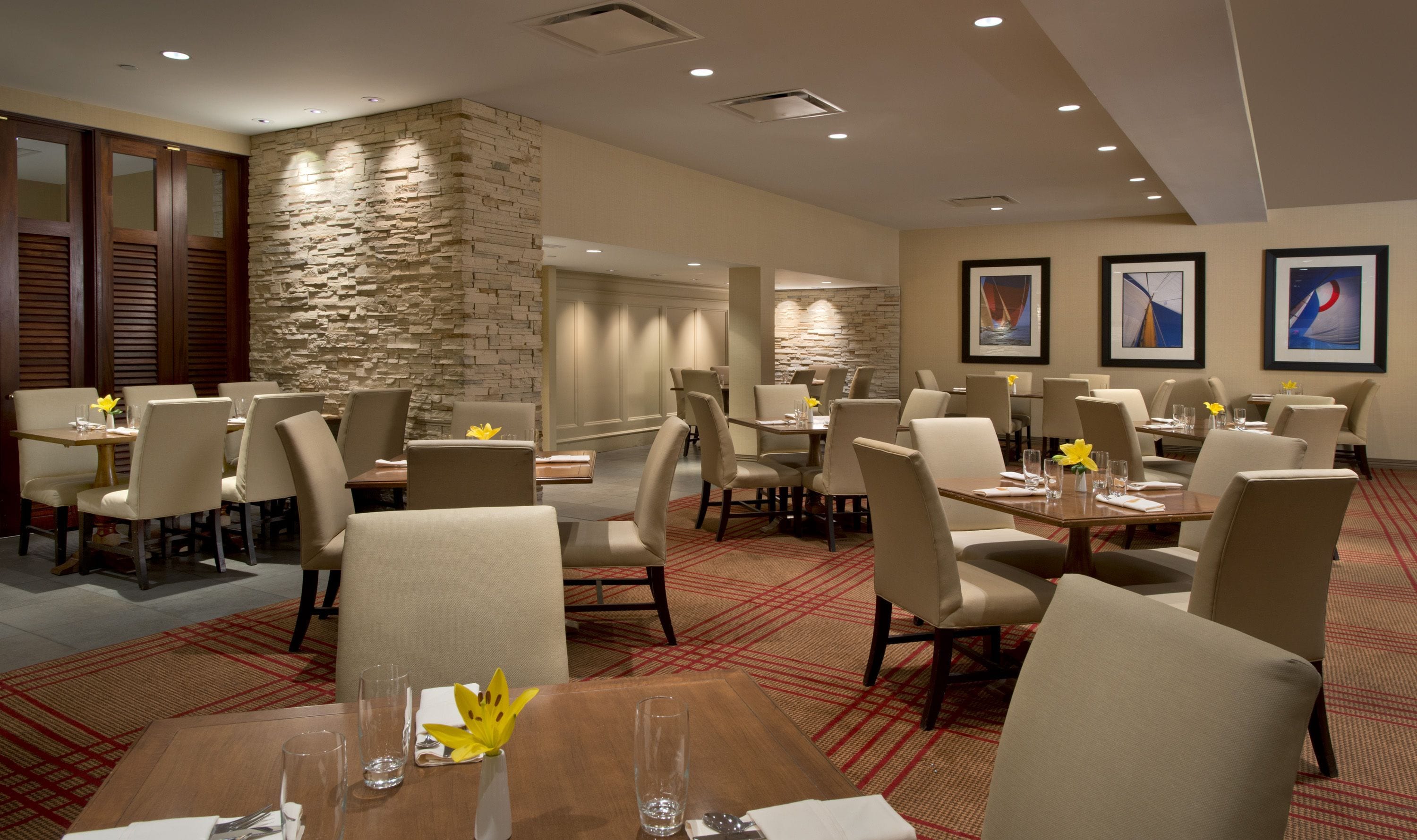 A hotel dining area with multiple tables and chairs, stone walls, and framed artwork on the walls.