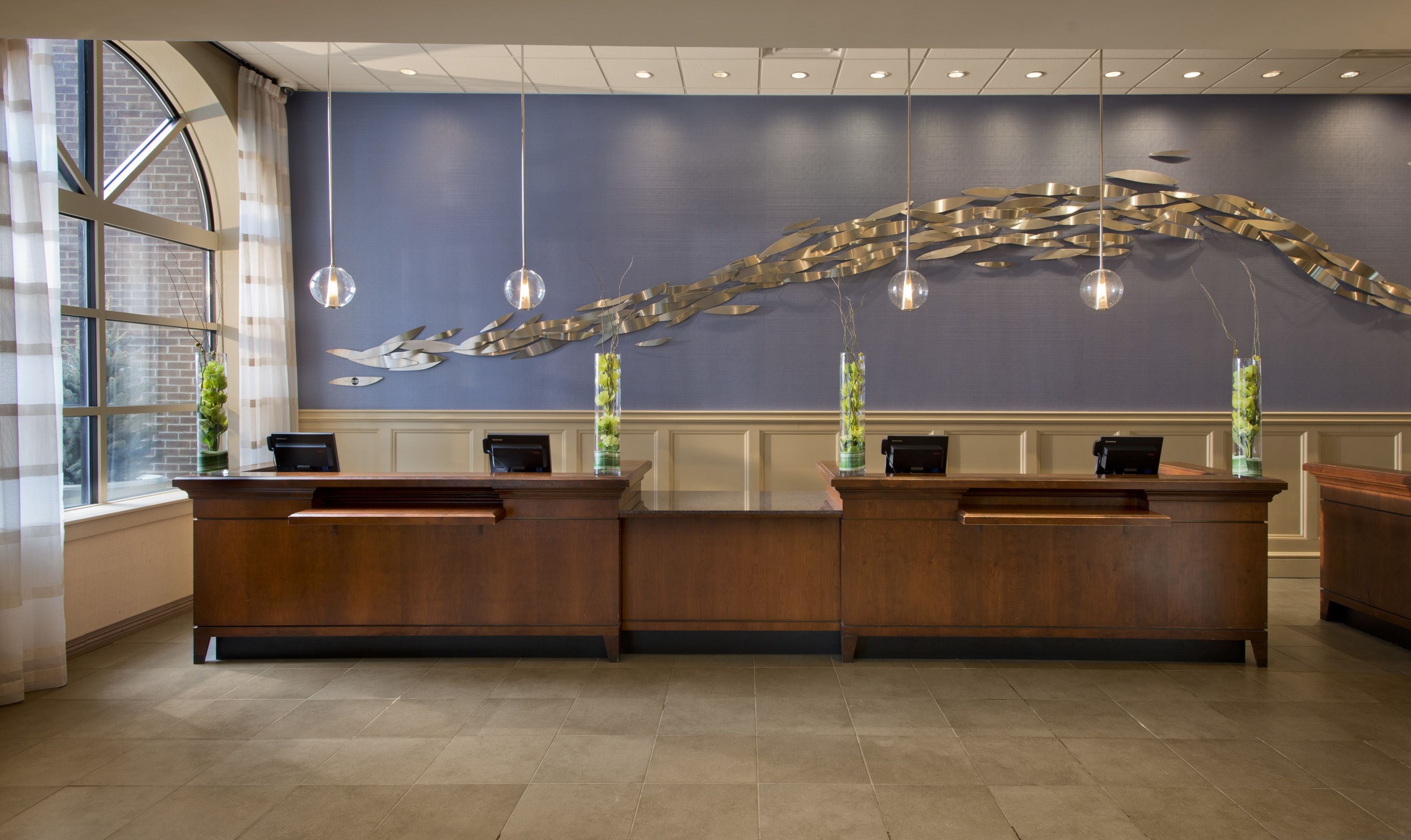 A reception desk with two counters, a blue wall with a metallic sculpture, and hanging pendant lights.