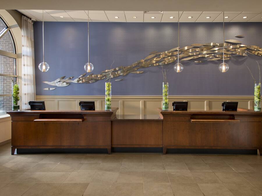 A reception desk with two counters, a blue wall with a metallic sculpture, and hanging pendant lights.