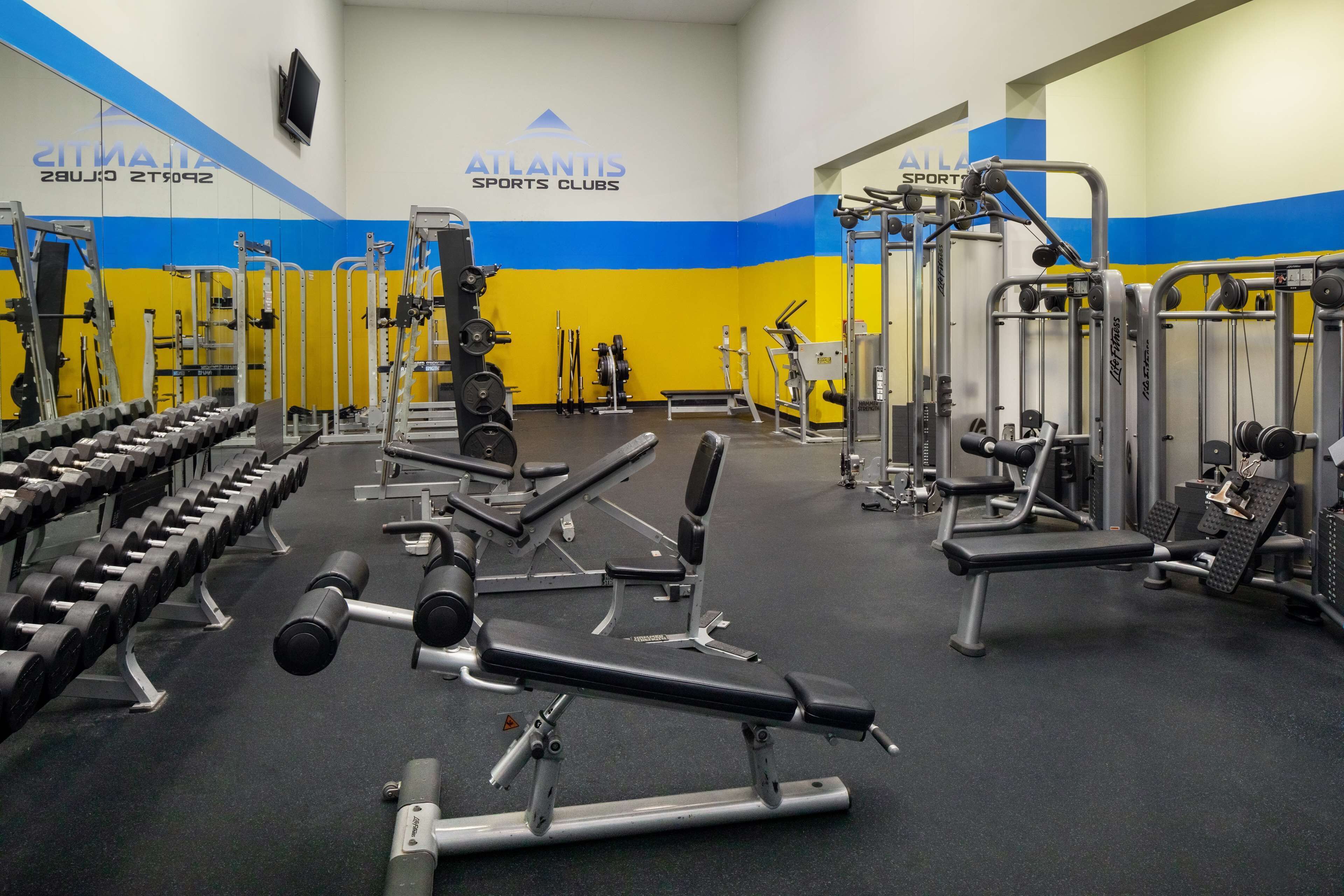Ein Fitnessstudio mit verschiedenen Trainingsgeräten, darunter Kurzhanteln, Bänke und Kraftgeräte.