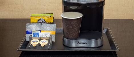 A coffee maker with a cup and tea bags on a tray.