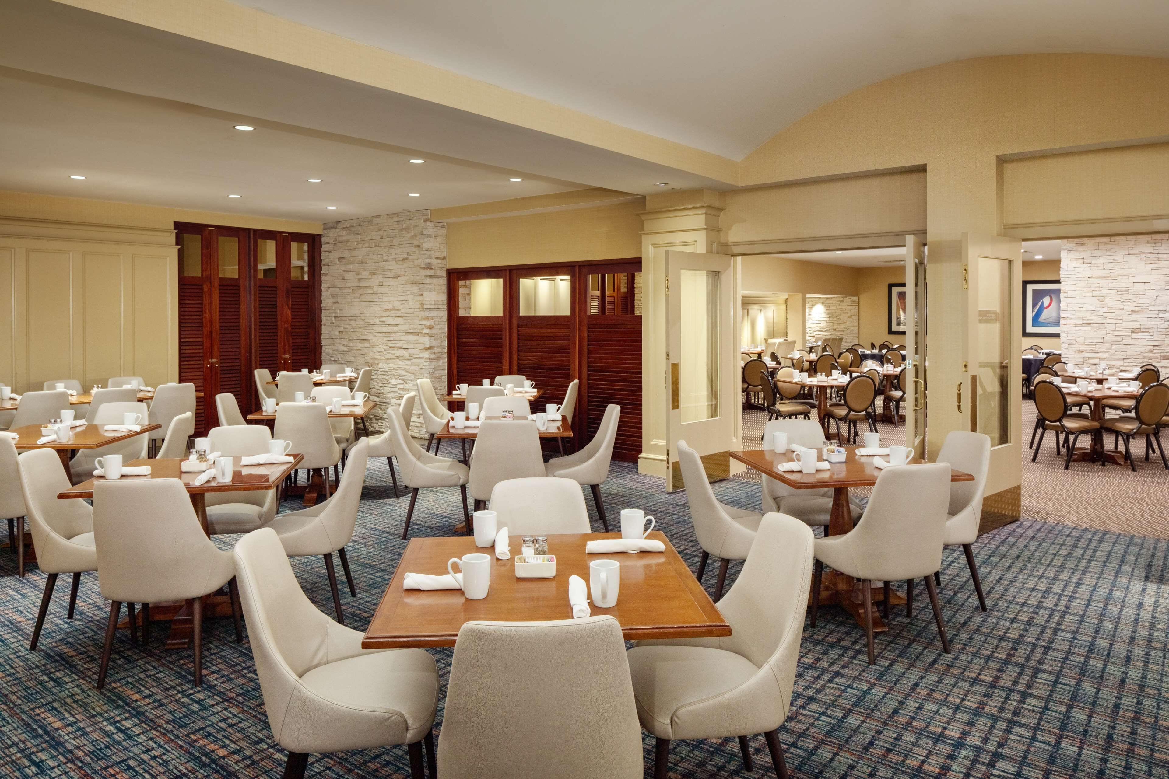 A hotel dining area with multiple tables and chairs, a stone accent wall, and wooden doors.