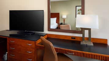 Ein Hotelzimmer mit Flachbildfernseher, Schreibtisch aus Holz, braunem Ledersessel, Spiegel und Nachttischlampe.