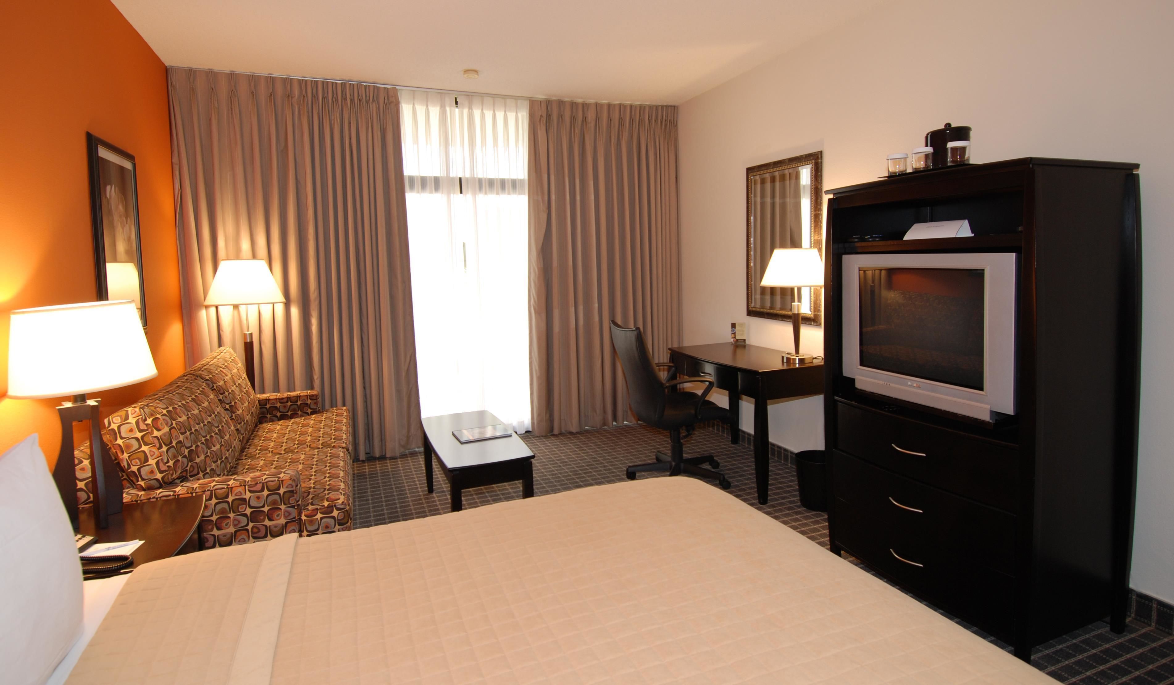 A hotel room with a bed, a desk, a chair, a television, and a lamp.