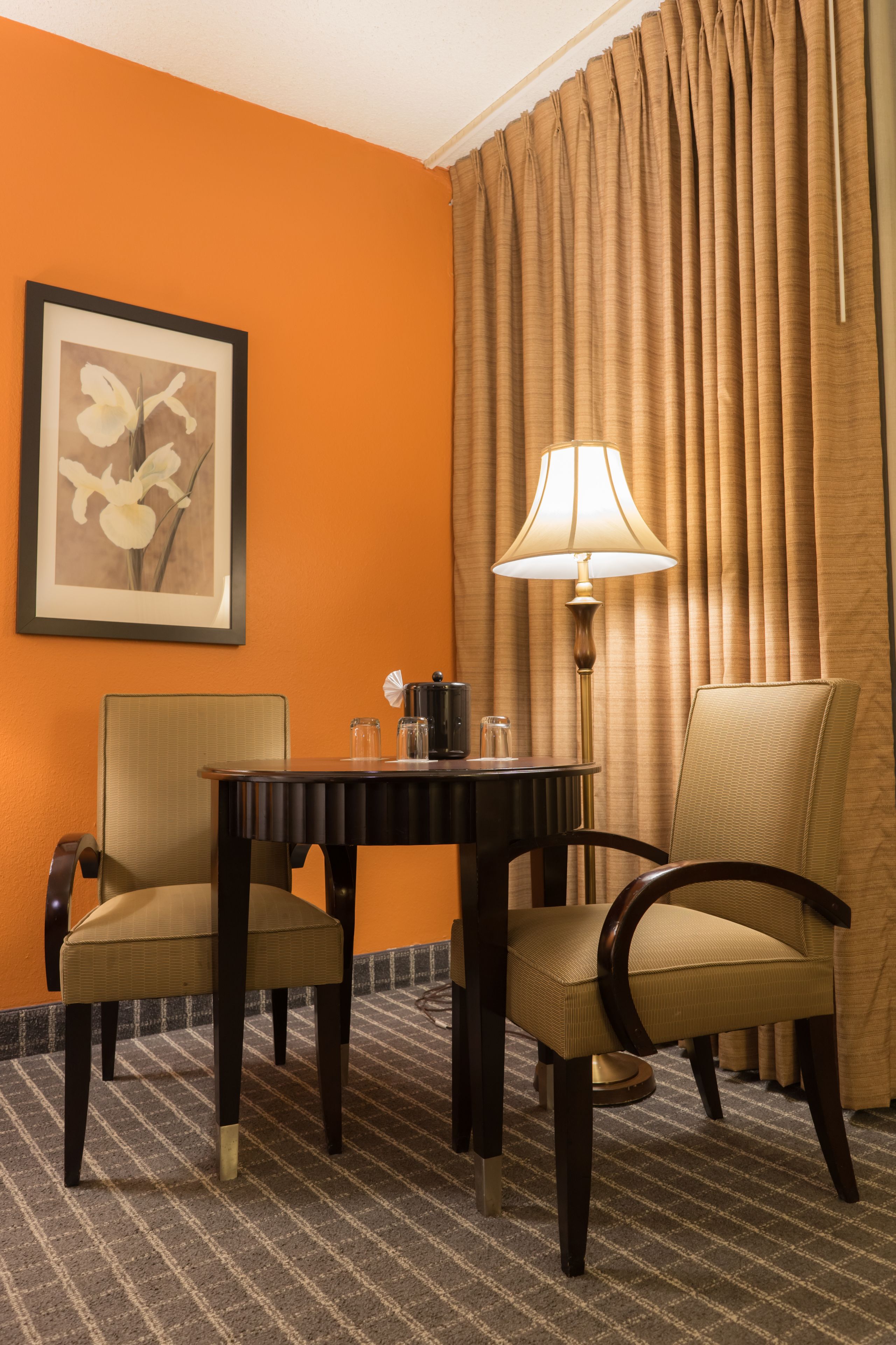 A hotel room with two chairs, a table, a lamp, and a framed picture on the wall.