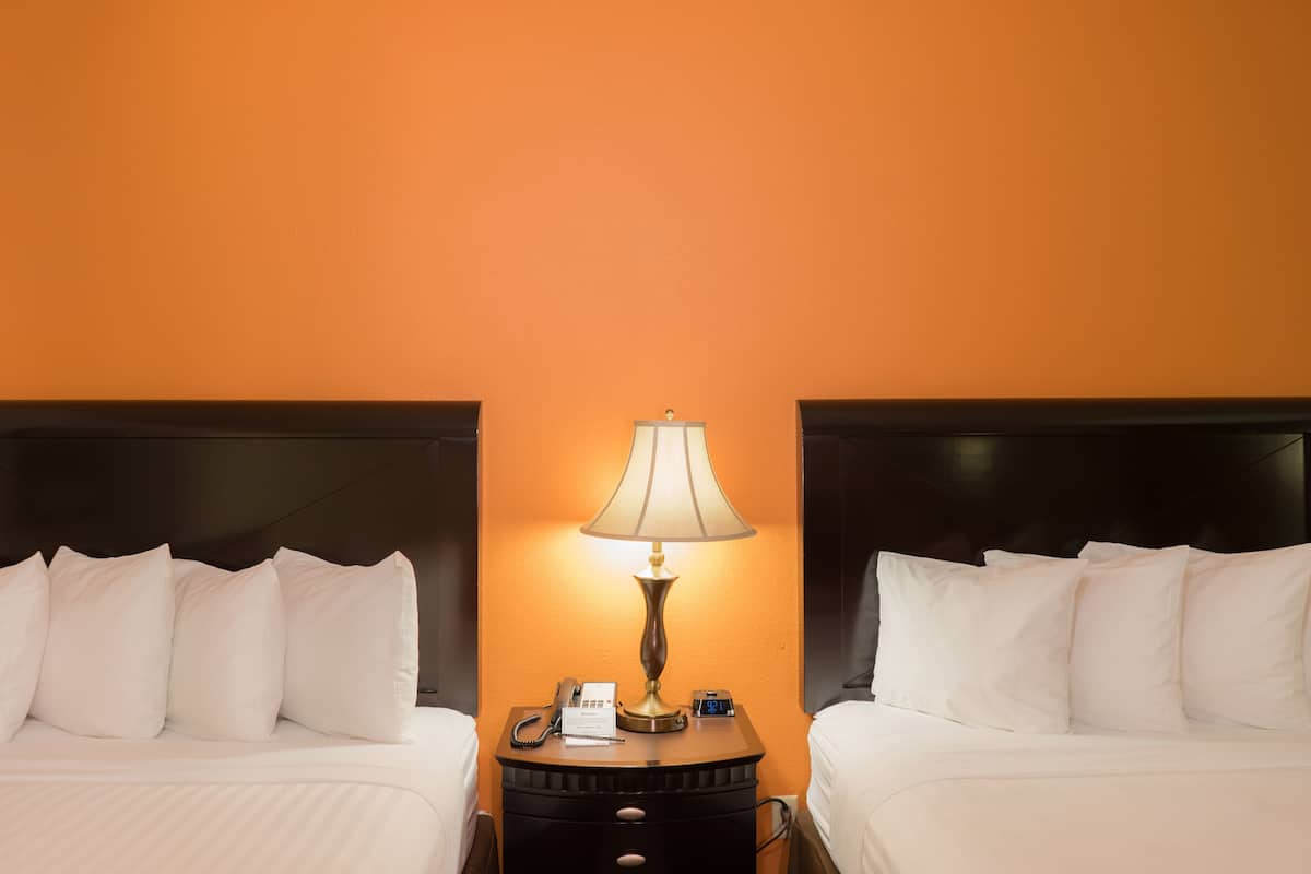 A hotel room with two beds, a nightstand with a lamp, a phone, and a digital clock.