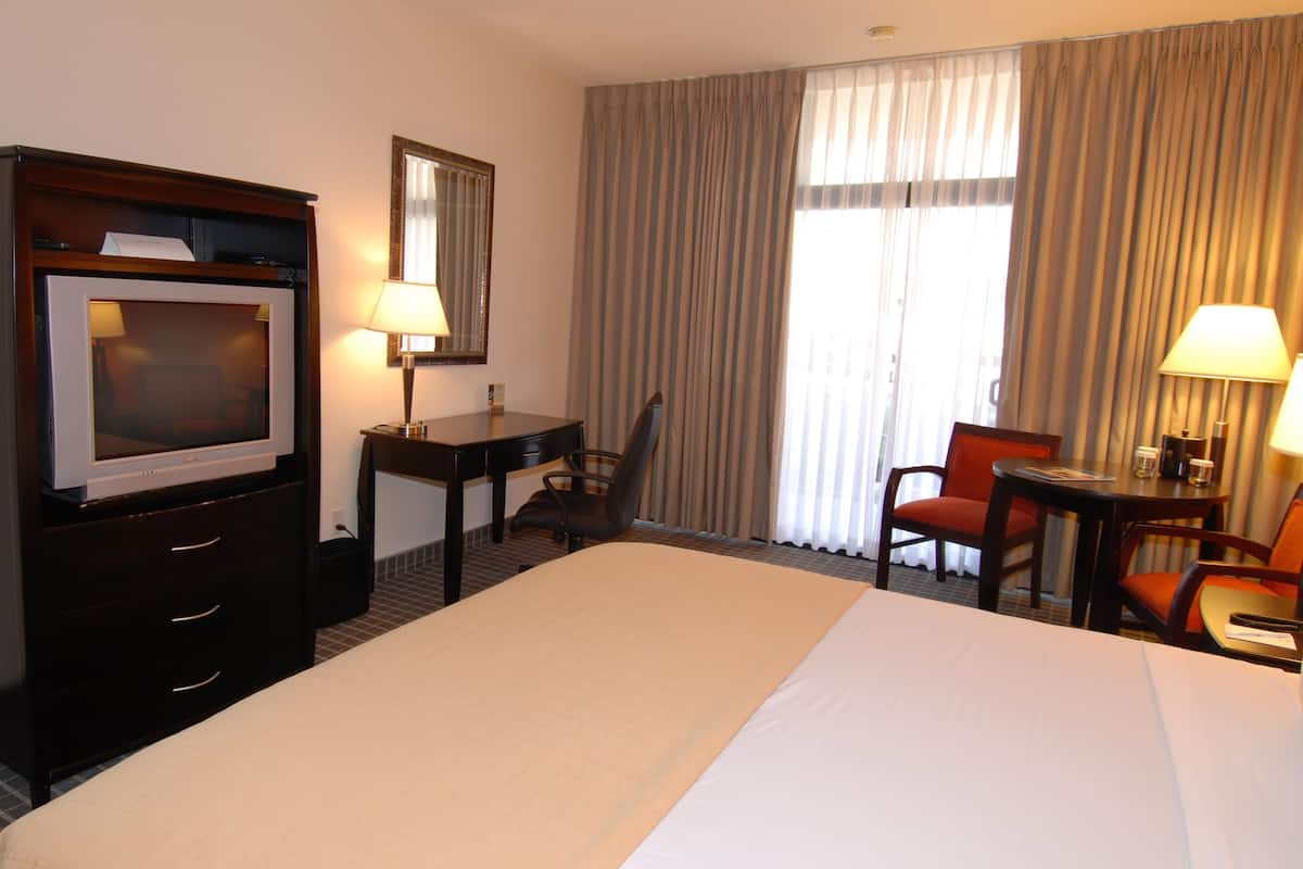 A hotel room with a large bed, a desk, a chair, a television, and two lamps.